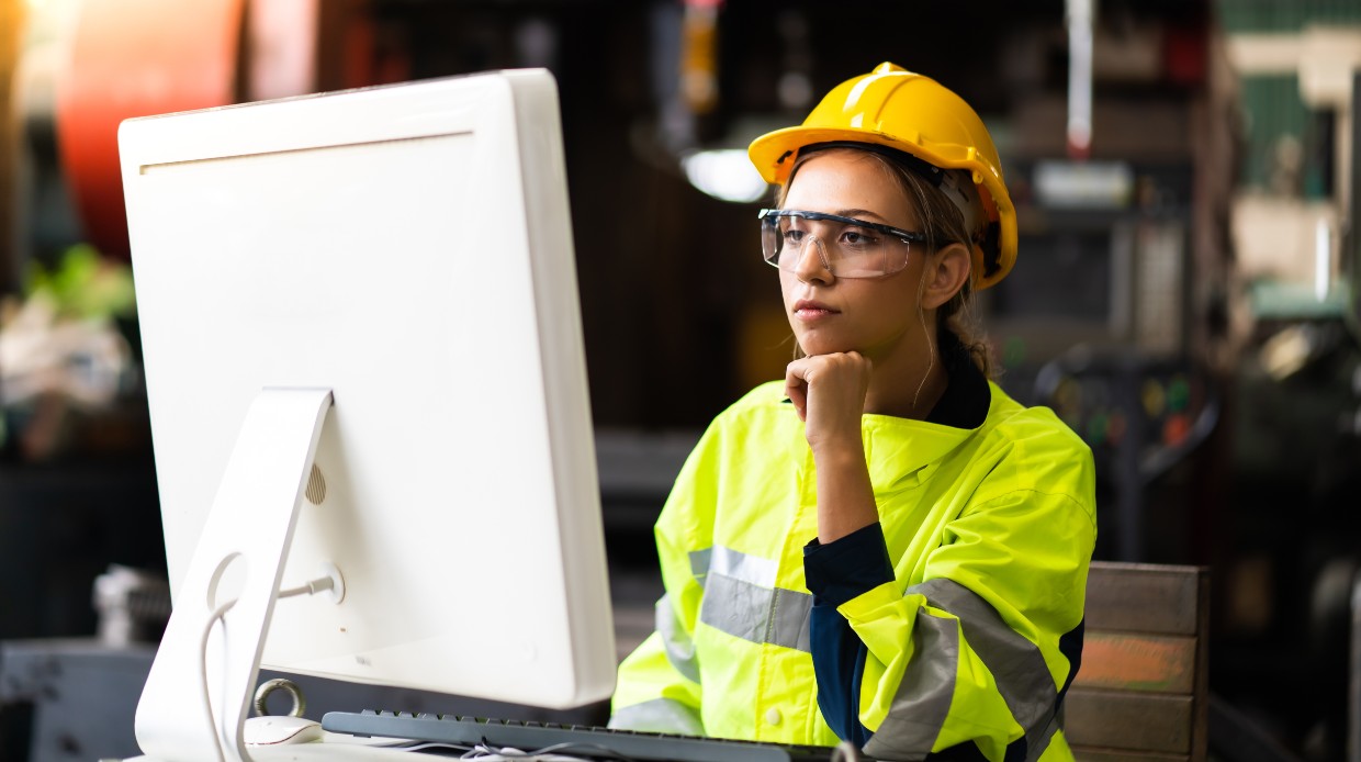 Woman engineer with a yellow hard hat working on desktop computer