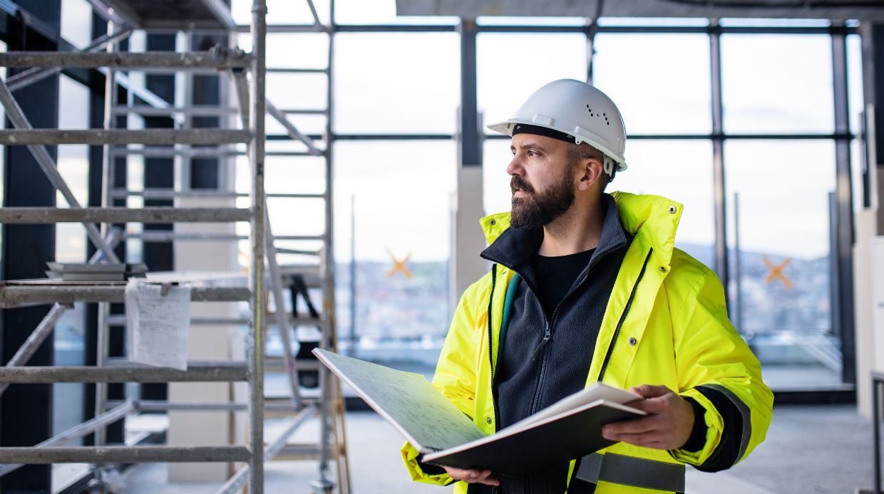 man engineer standing on construction site, holding blueprints and making better business decisions